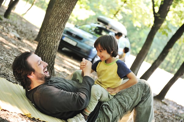 Happy family, father and son in focus, and behind them out of the focus mother and child and their car