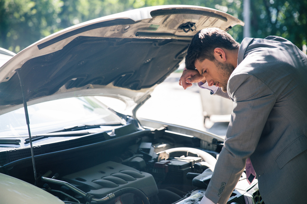 man looking at engine of car with concern